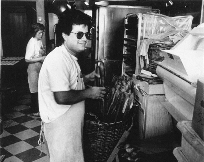 Black and white photo of man placing baguettes in basket